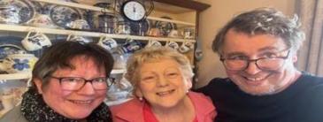 Two women and one man smiling in front of a dresser